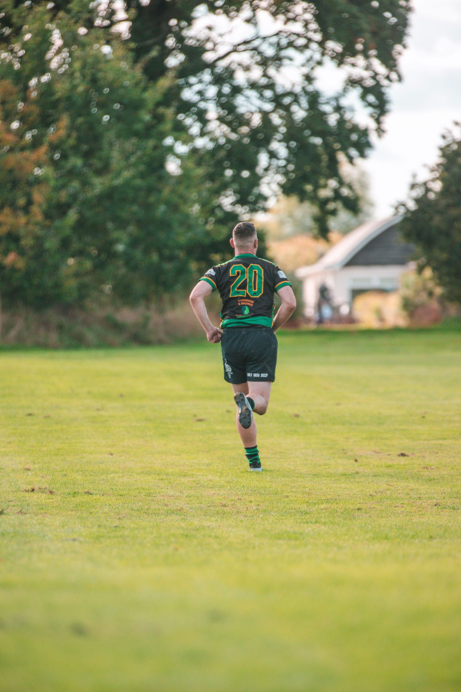 Rugby player wearing jersey number 20 running alone across green sports field.