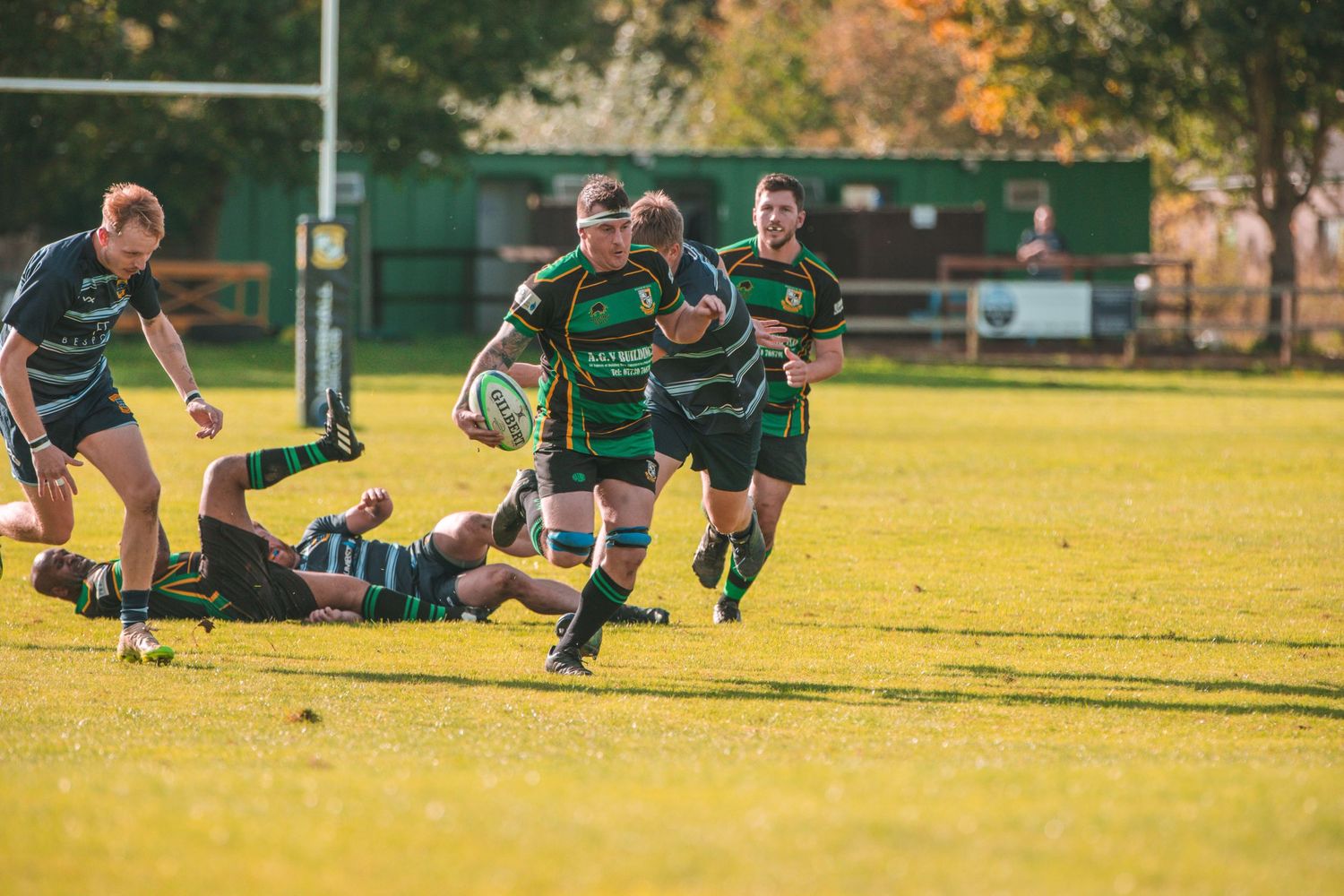 Rugby players in green jerseys making a break during competitive match on sunny field.