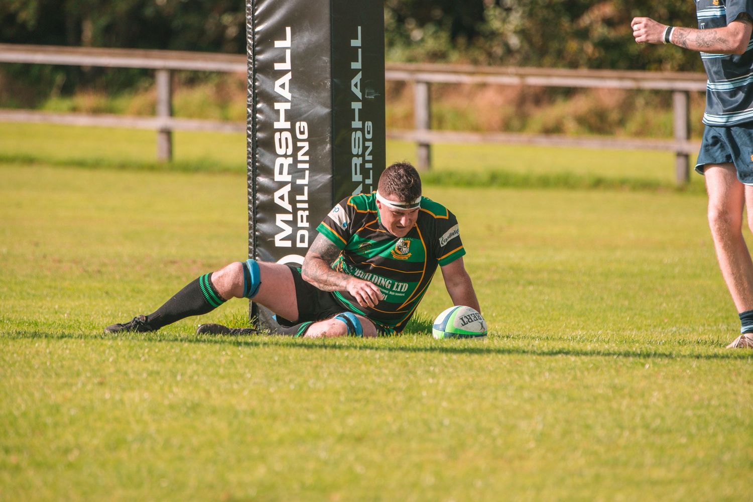 Rugby player in green and black striped jersey sits on grass field during match.