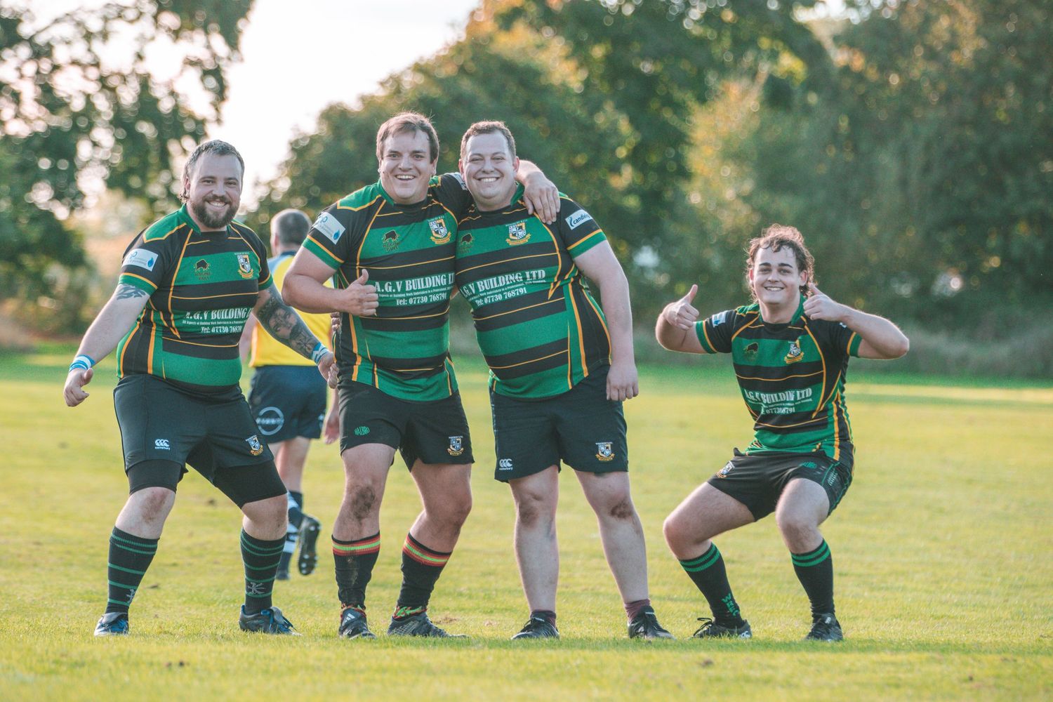 Rugby team players pose playfully in green and black striped uniforms on sunny field.