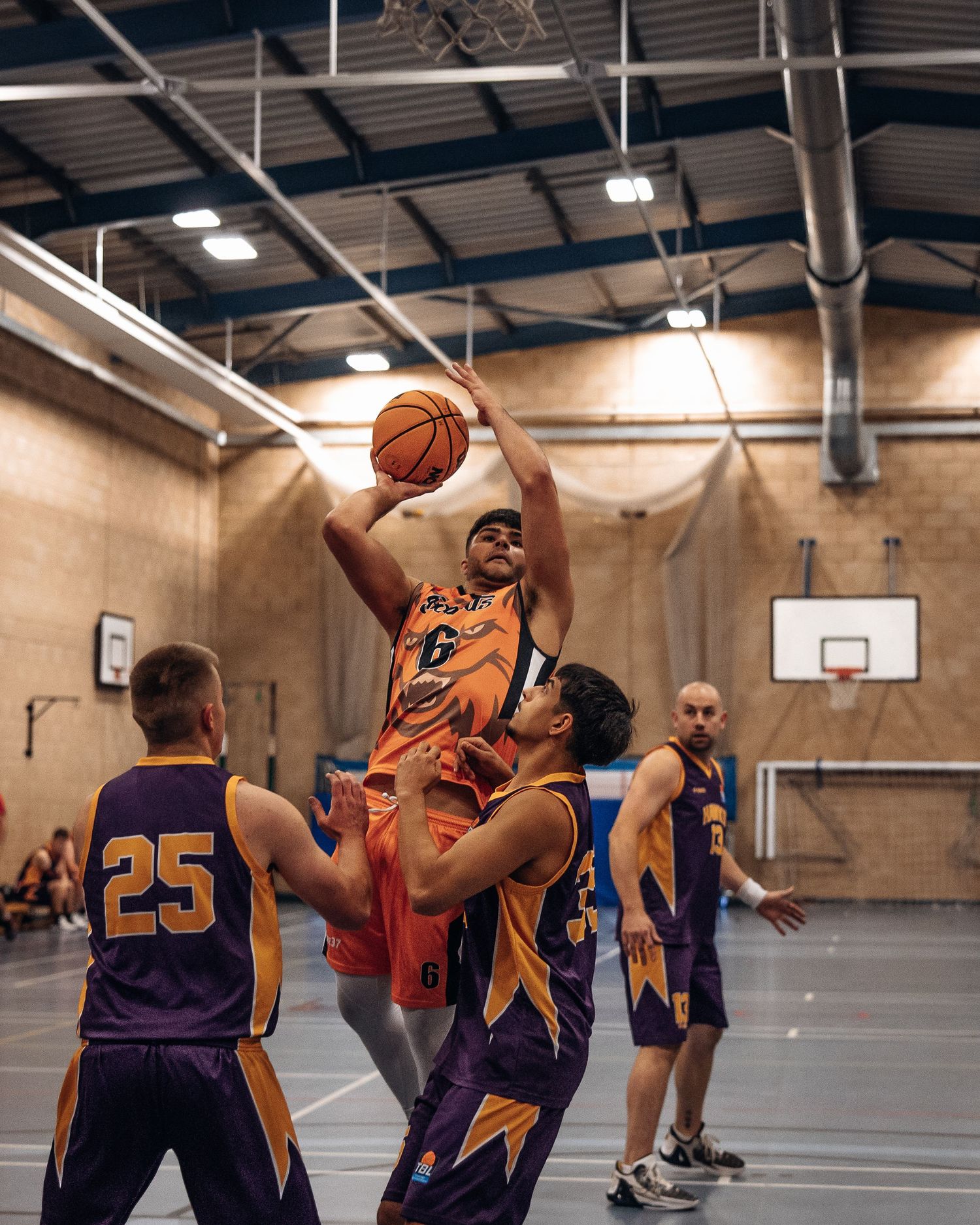 Basketball player in orange jersey leaps high for a shot during an indoor game.
