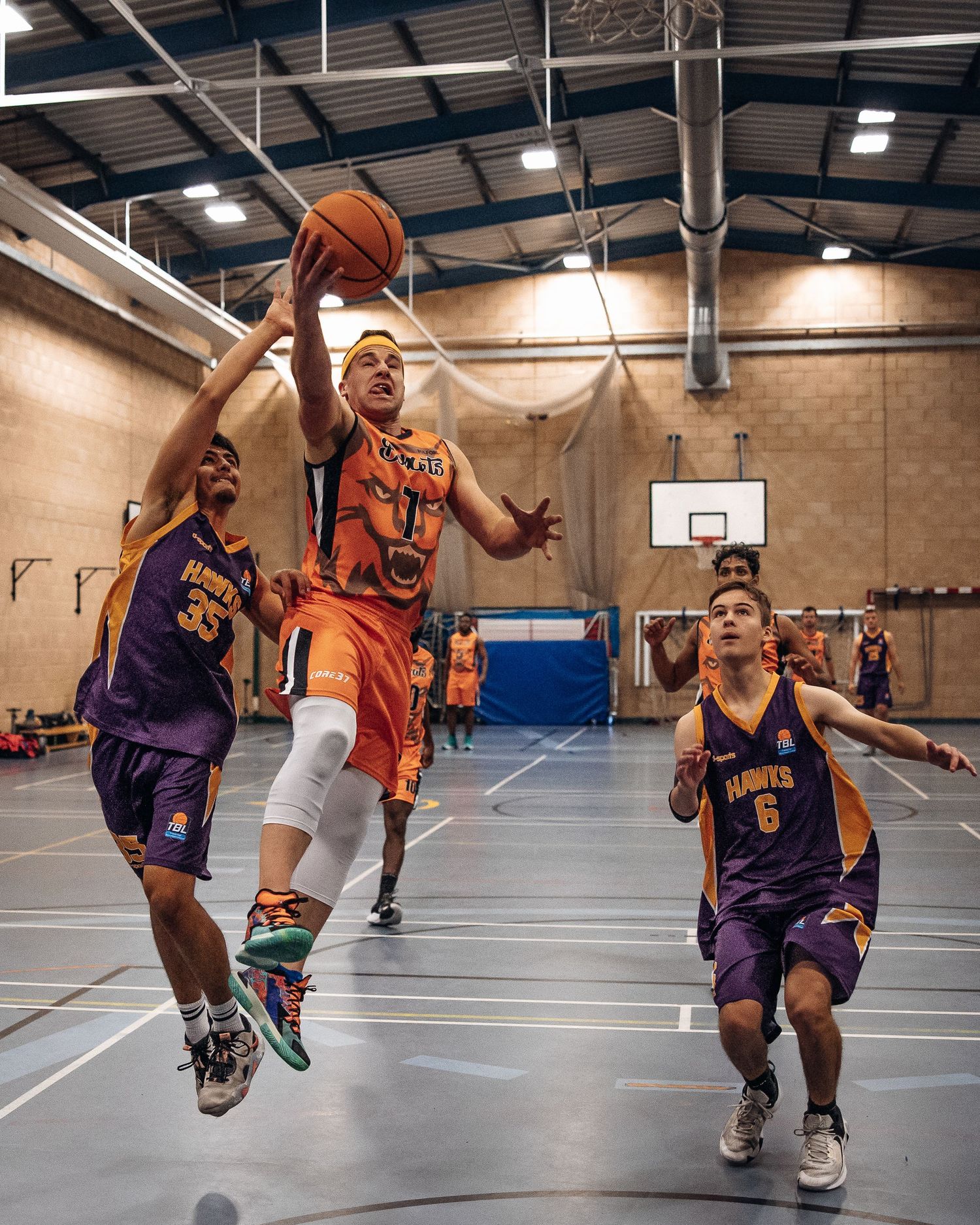 Basketball player in orange jersey attempts a layup while being defended.