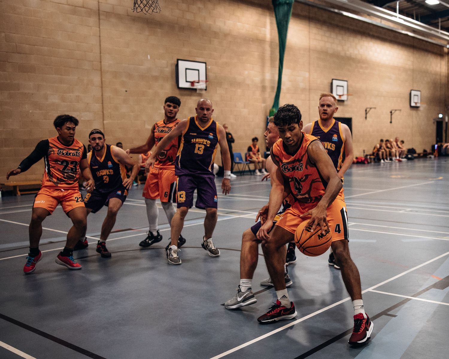 Competitive indoor basketball game between teams in orange and purple jerseys.