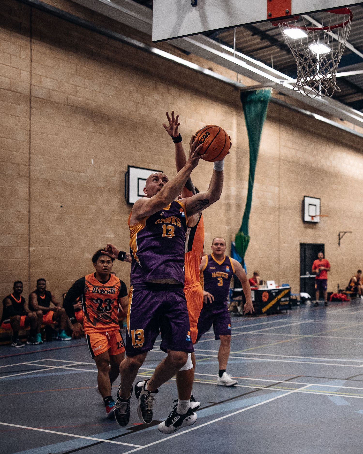 Basketball player in purple jersey attempts shot while being defended in indoor game.