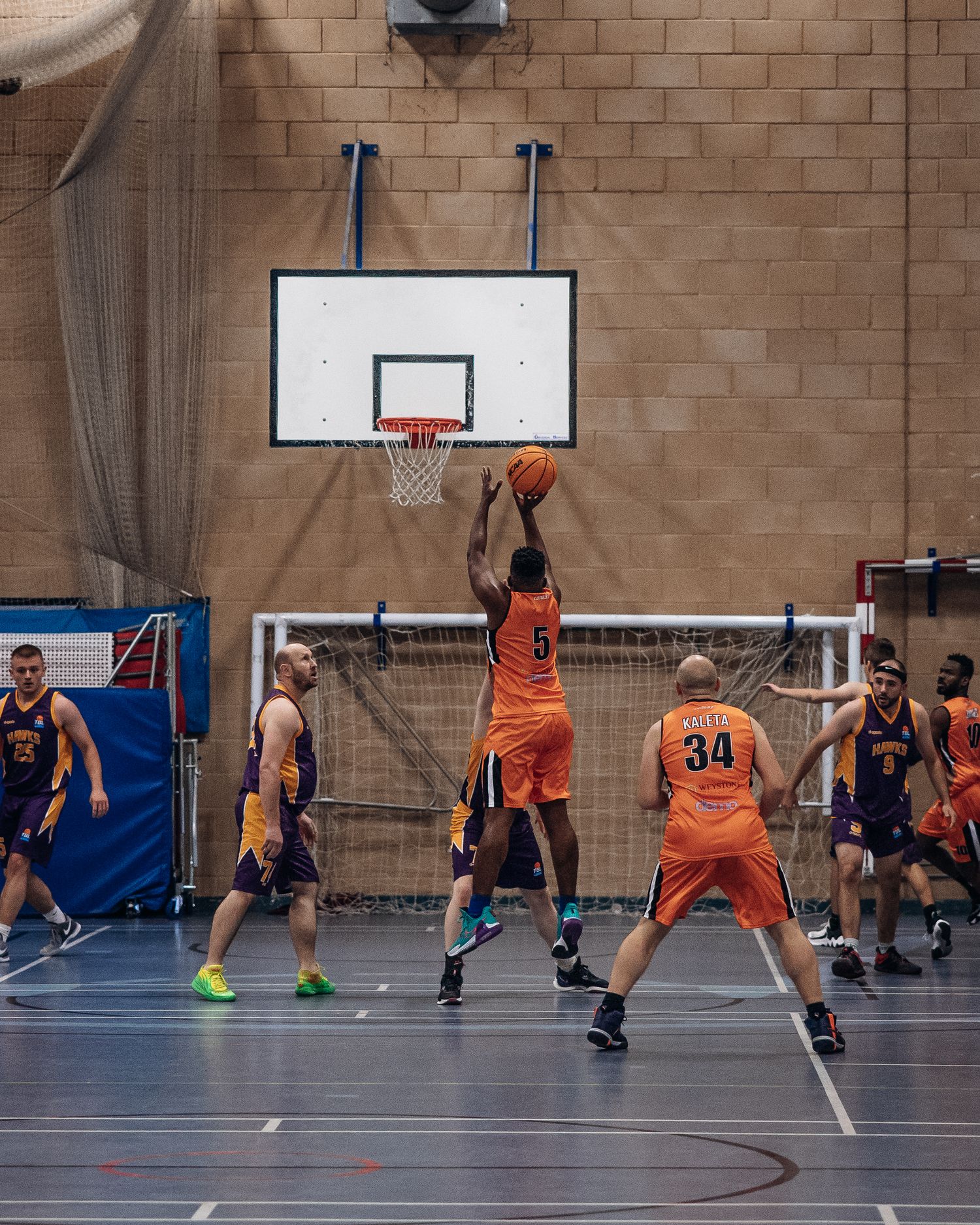 Basketball player in orange jersey attempts a layup during indoor game with opponents defending.
