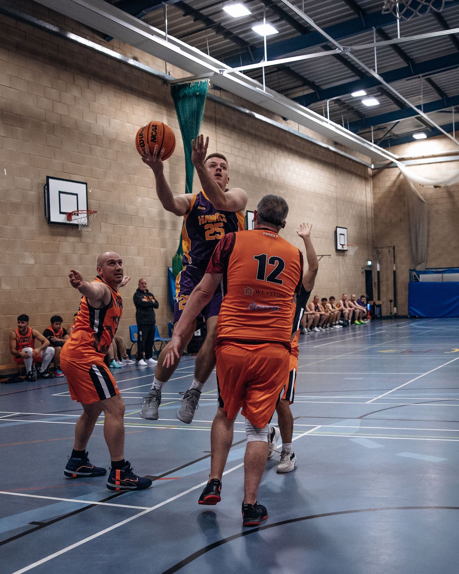 Basketball player leaps for a shot while being defended by players in orange jerseys.