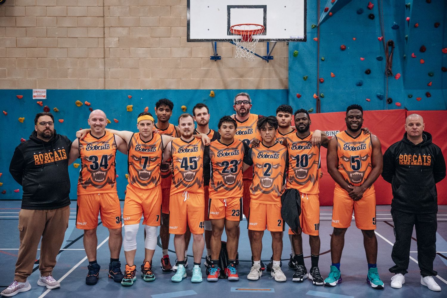 Team photo of basketball players in orange uniforms standing together in indoor court.
