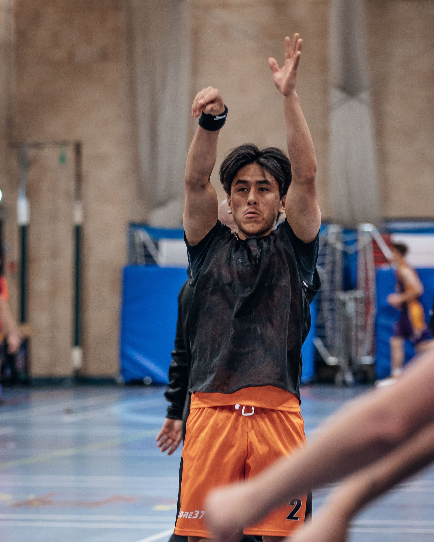 Basketball player in orange uniform signals during indoor game with arms raised.