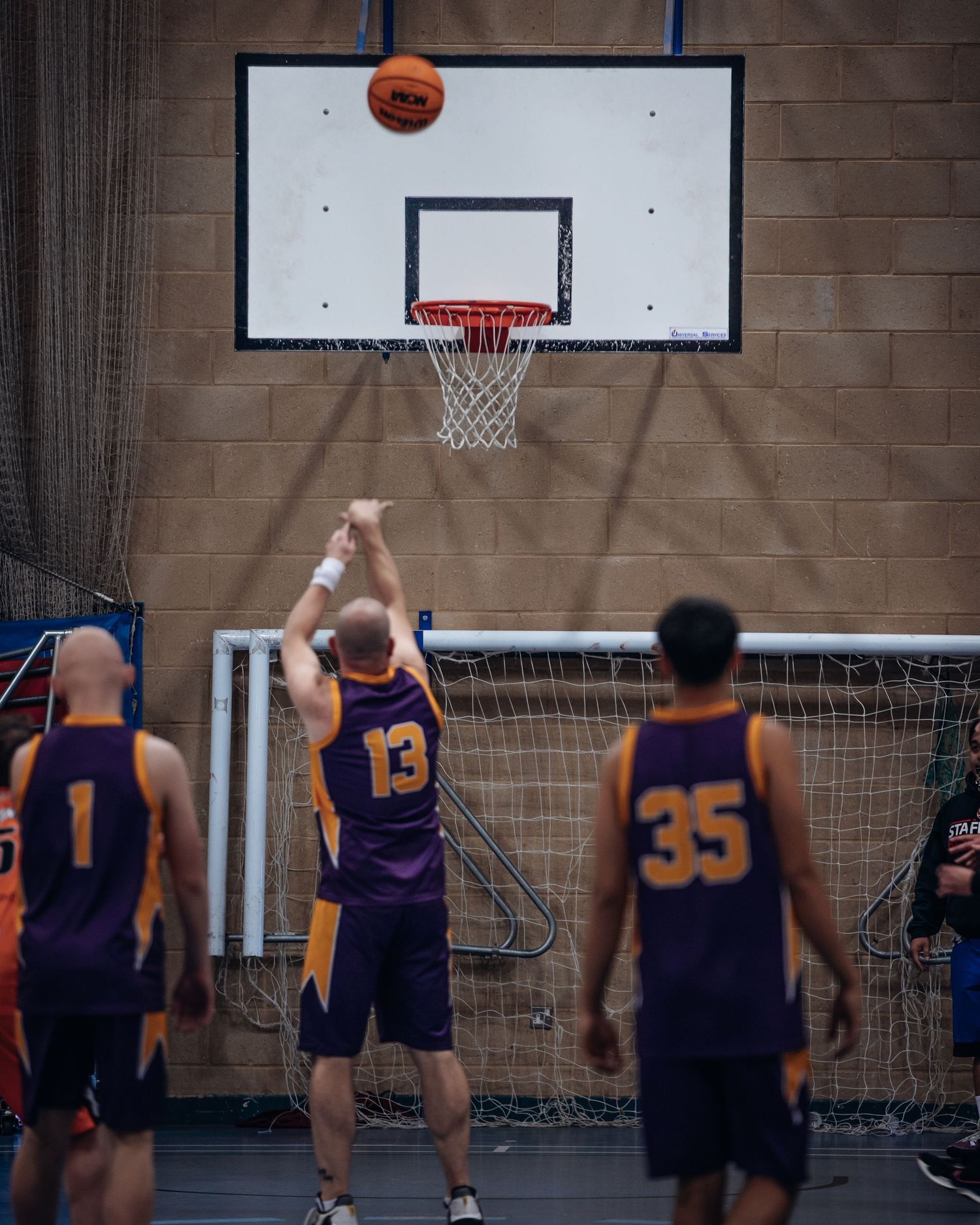 Basketball player in purple jersey takes a shot at indoor court basket.