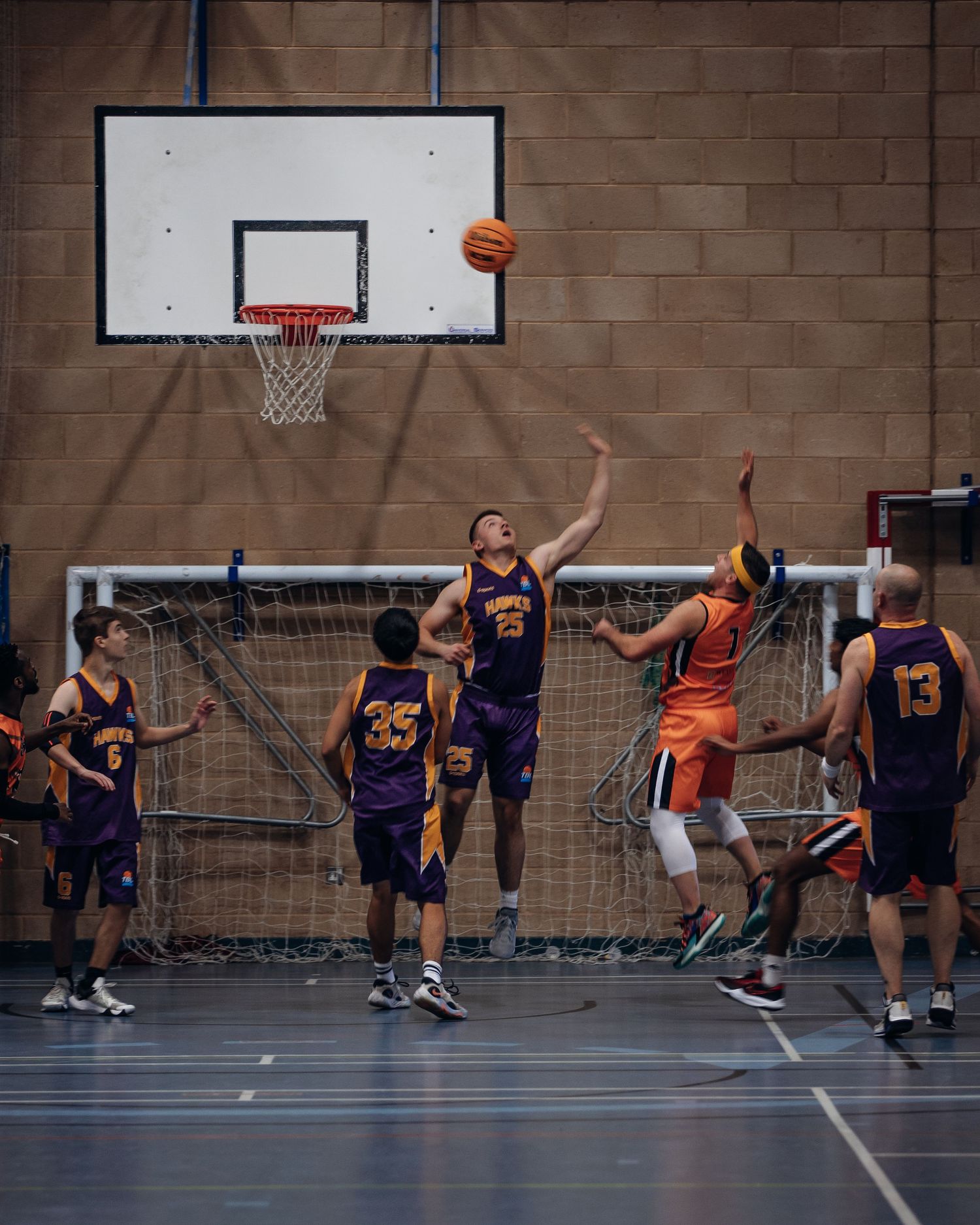 Basketball players from opposing teams jump for the ball during indoor game.