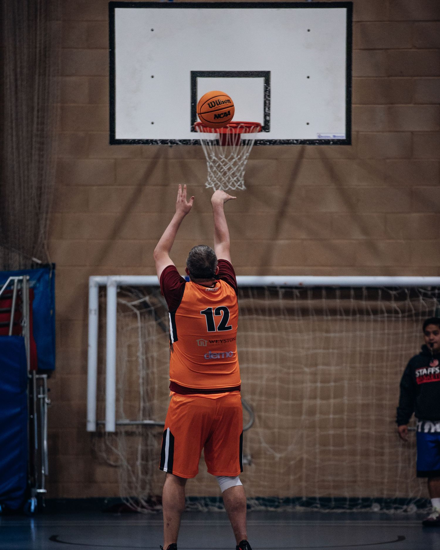 Player in orange jersey shoots basketball at hoop during indoor game.