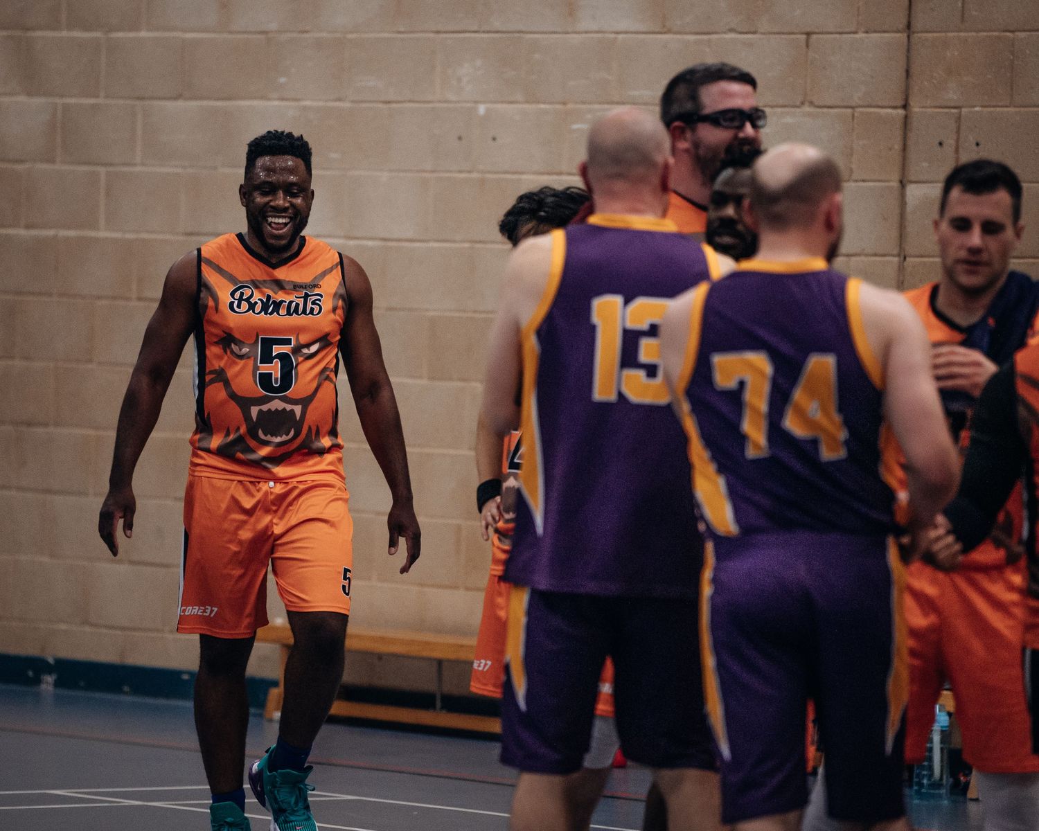 Players from opposing teams in orange and purple jerseys interact during basketball game.