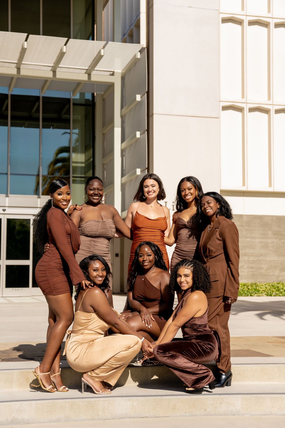 A group in coordinated brown and beige outfits poses together on outdoor steps for a stylish photoshoot.