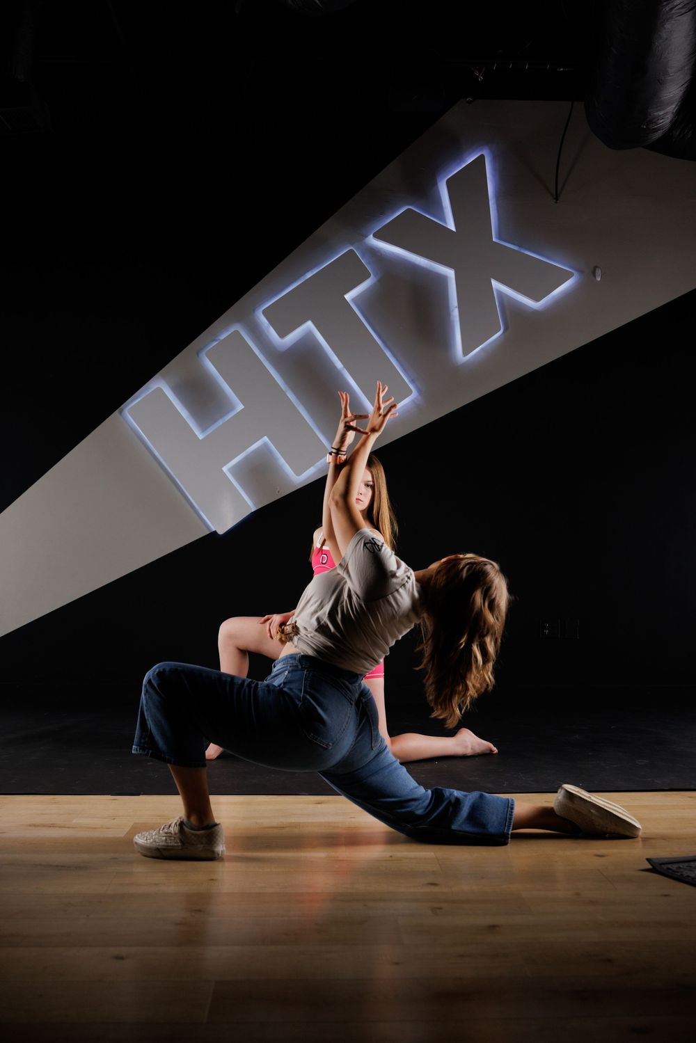 Emily Roy posing a dancer on a wooden floor beneath a glowing HTX projection at The Dance Barre HTX.
