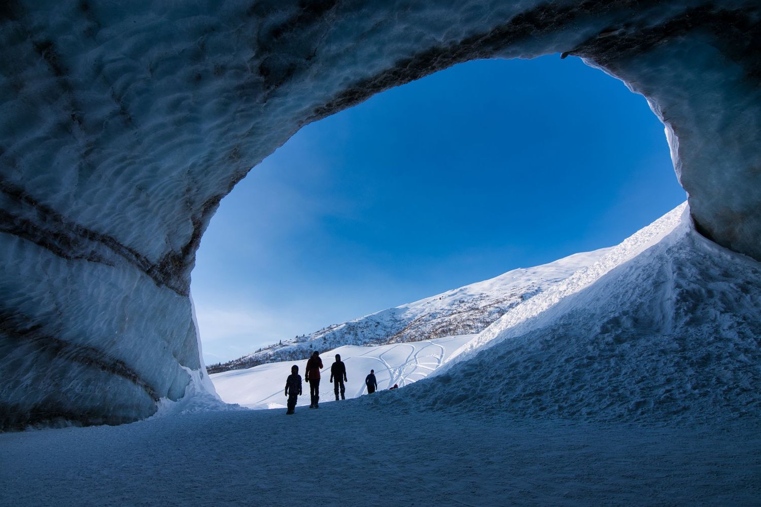 View from within ice cave in Alaska with silhouette of family and a blue sky.