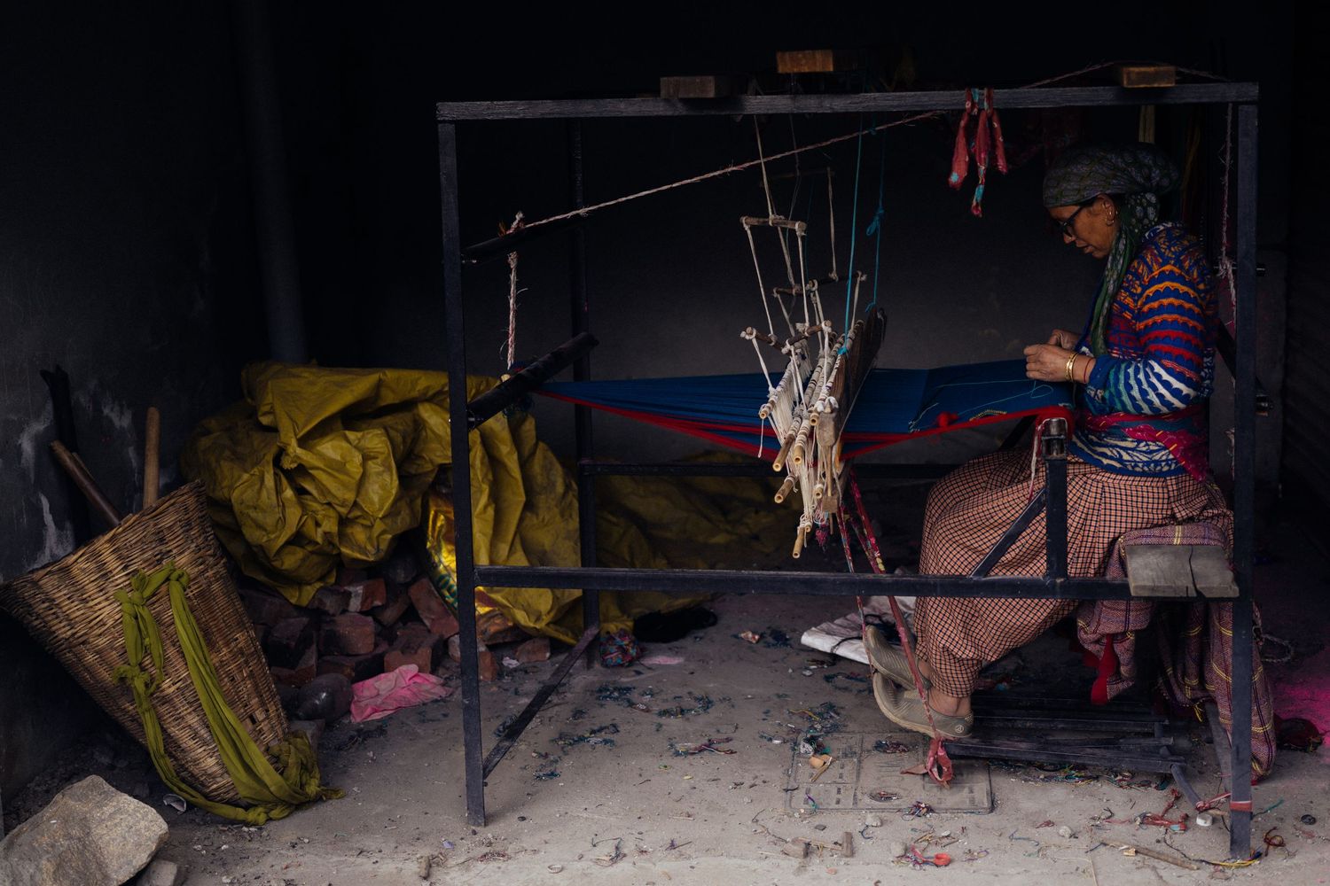 Person in striped clothing tending to hanging meat in dark rustic cooking space.
