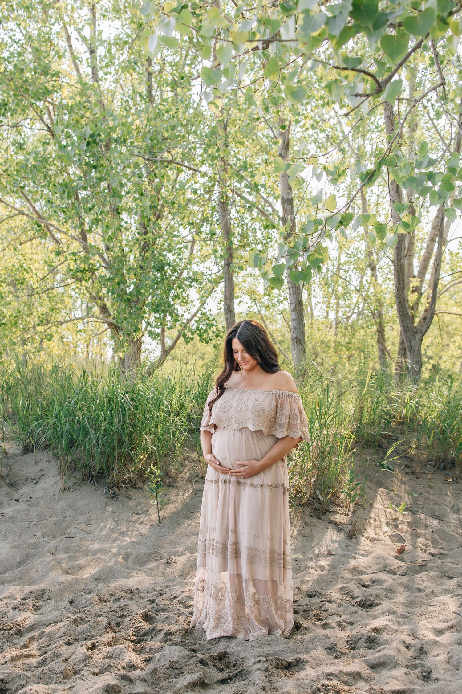 Maternity photo showing white lace dress and burgundy hat in golden field at sunset.