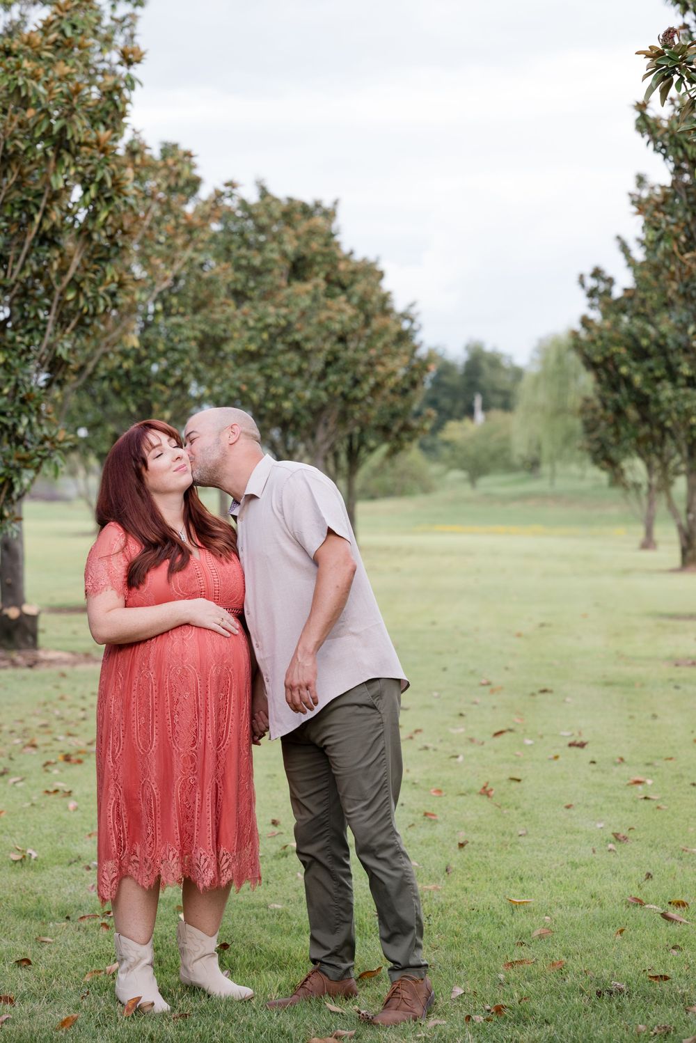 A couple shares an intimate moment in a park setting with trees in the background.