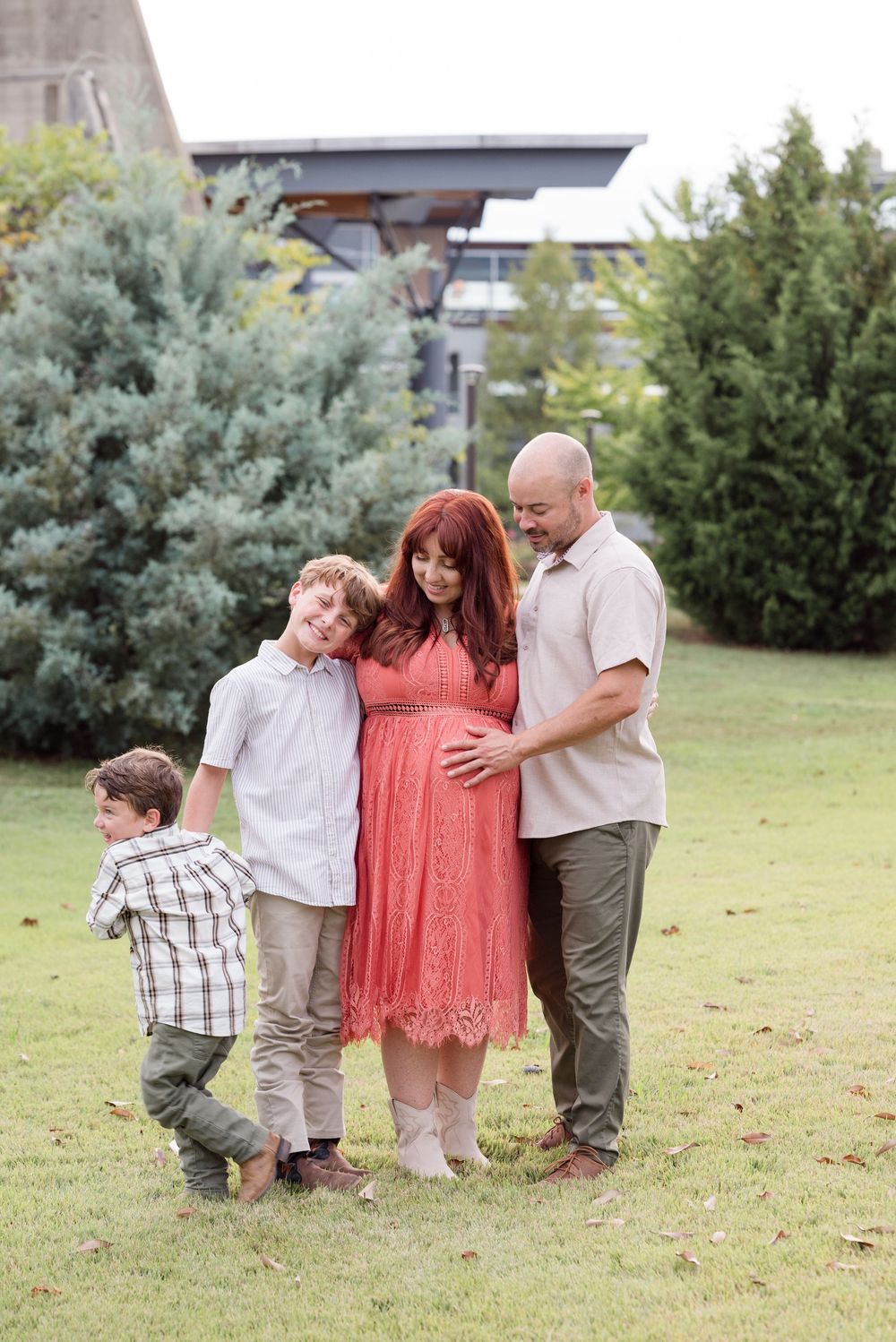 A family group poses together on grass with modern architecture in the background.