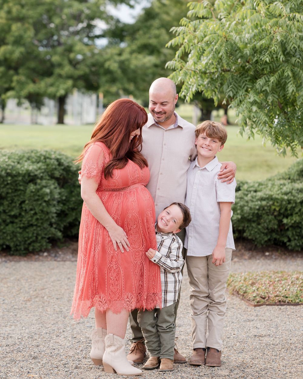 A family poses together outdoors in a park setting with green trees and bushes in the background.