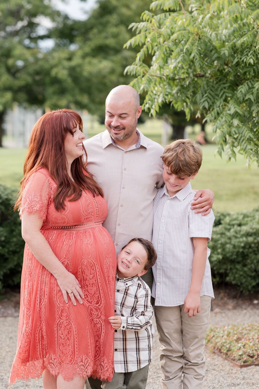 A cheerful family shares a candid moment together while posing near leafy trees in a garden setting.