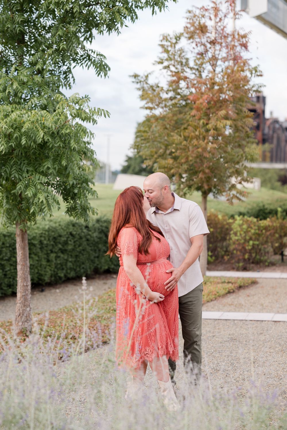 A couple shares an intimate moment outdoors as they celebrate an expected arrival in a coral lace maternity dress.