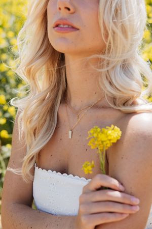Close up portrait of someone with blonde hair and white top against yellow flower background.