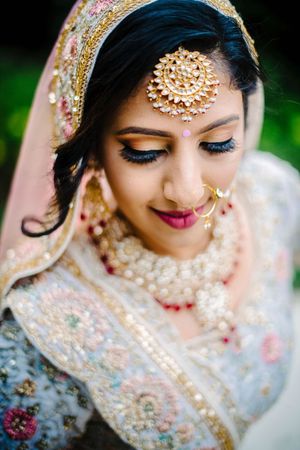 Close up detail of traditional South Asian bridal makeup and jewelry with ornate gold headpiece.