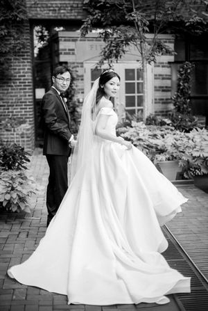 A black and white wedding portrait of a couple on a brick patio with a bride wearing a flowing white gown.
