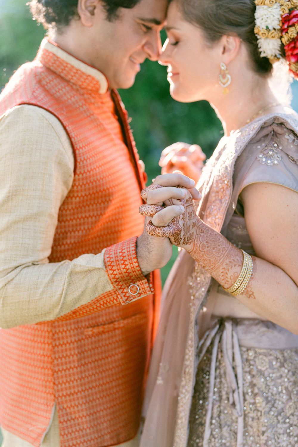 Close-up shots of a couple in traditional Indian wedding attire with orange and silver details embracing tenderly outdoors.
