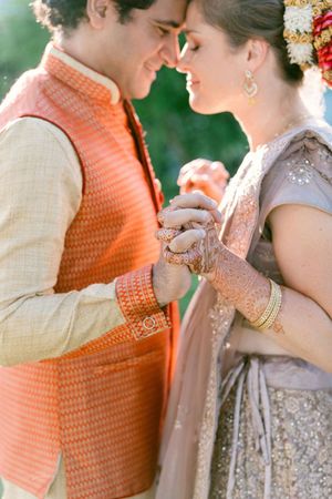 Close-up shots of a couple in traditional Indian wedding attire with orange and silver details embracing tenderly outdoors.