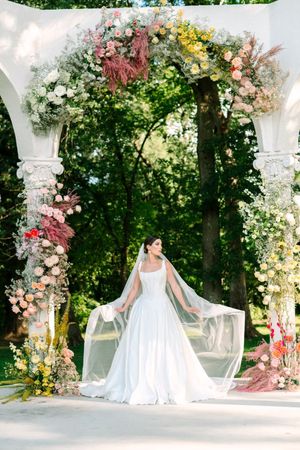 A wedding dress displayed in a garden setting with floral arches and natural greenery creating a romantic outdoor backdrop.