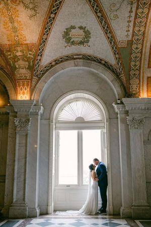 A romantic wedding silhouette in an ornate historic building with classical columns and a stunning arched window.