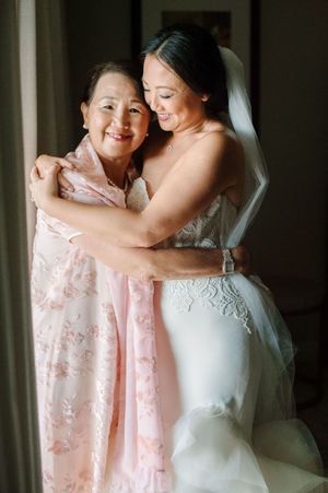 A tender moment shared between mother and daughter embracing while wearing pink and white dresses for a wedding.
