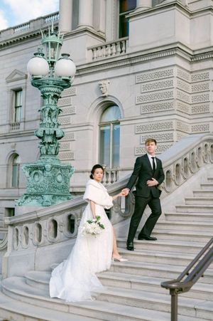 A wedding couple poses on ornate marble steps of a historic building with decorative verdigris lamp post in elegant setting.