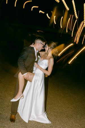 A couple dances together at a wedding reception with sparklers creating light trails in the dark background.