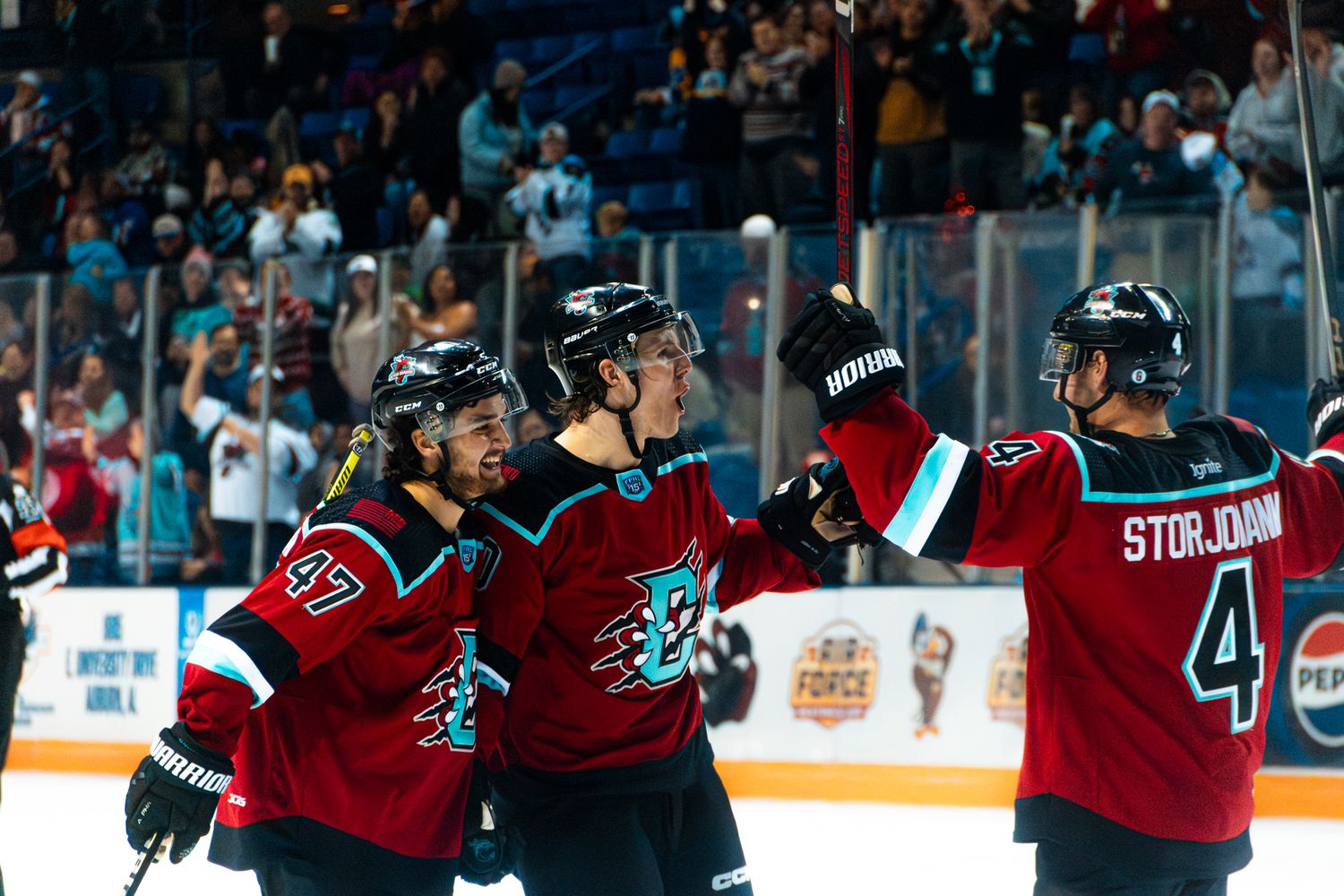 Hockey player in dark jersey with teal and red accents skates on ice during competitive game.