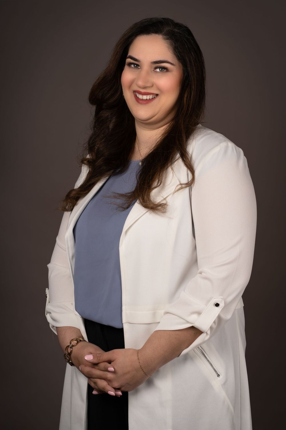 Professional headshot wearing white blazer and blue top with confident pose.