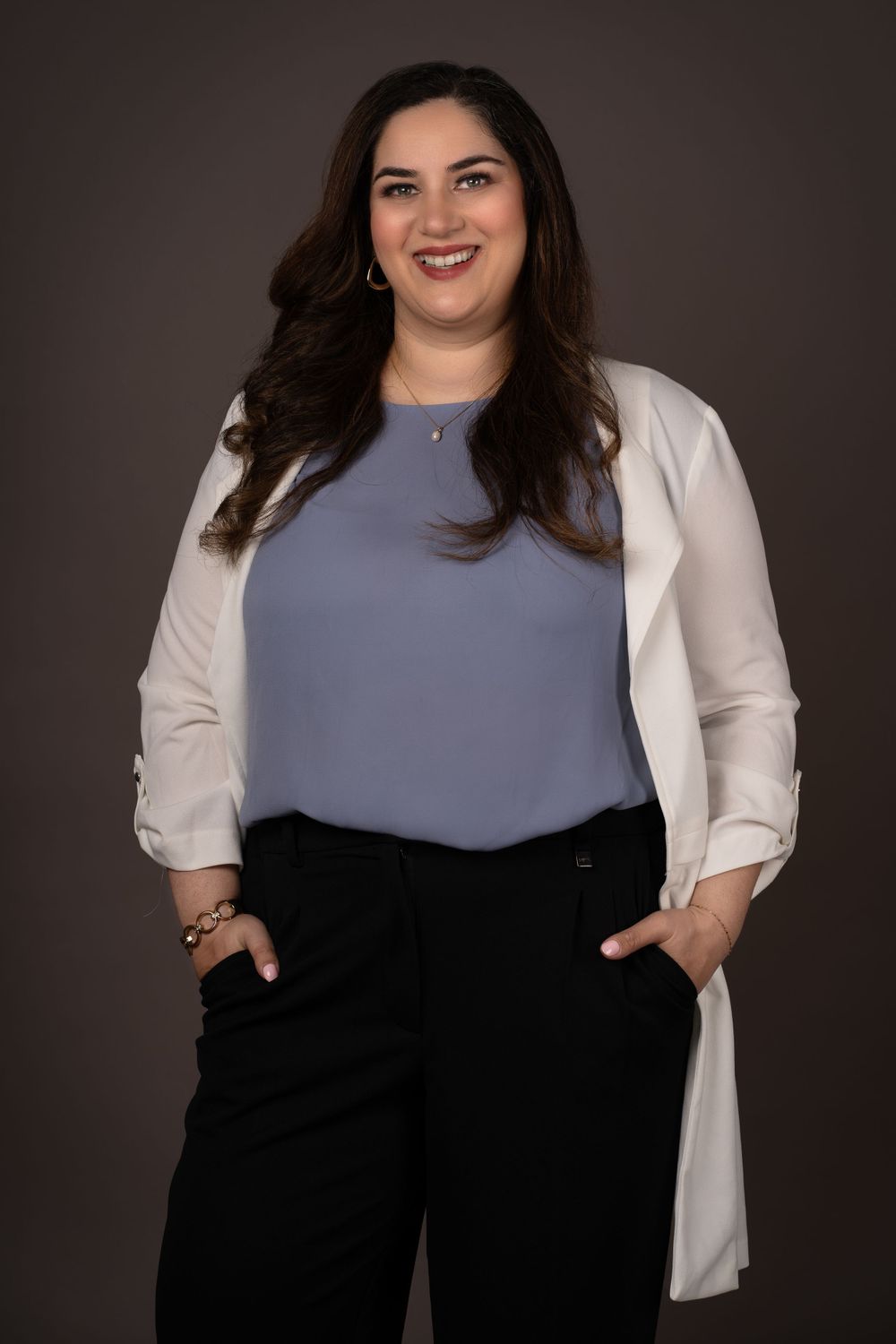 Professional portrait in business attire with white blazer and gray top against dark background.