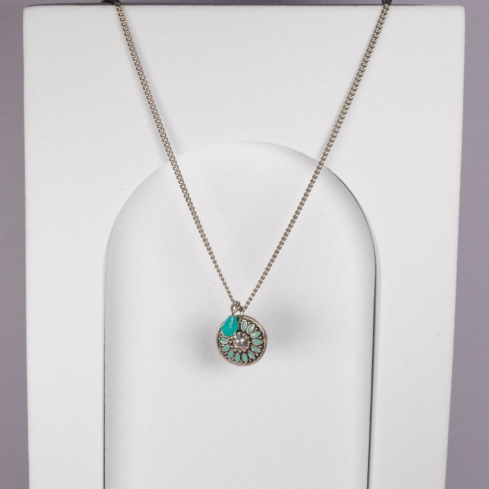 Turquoise circular pendant necklace with silver chain on white display stand.