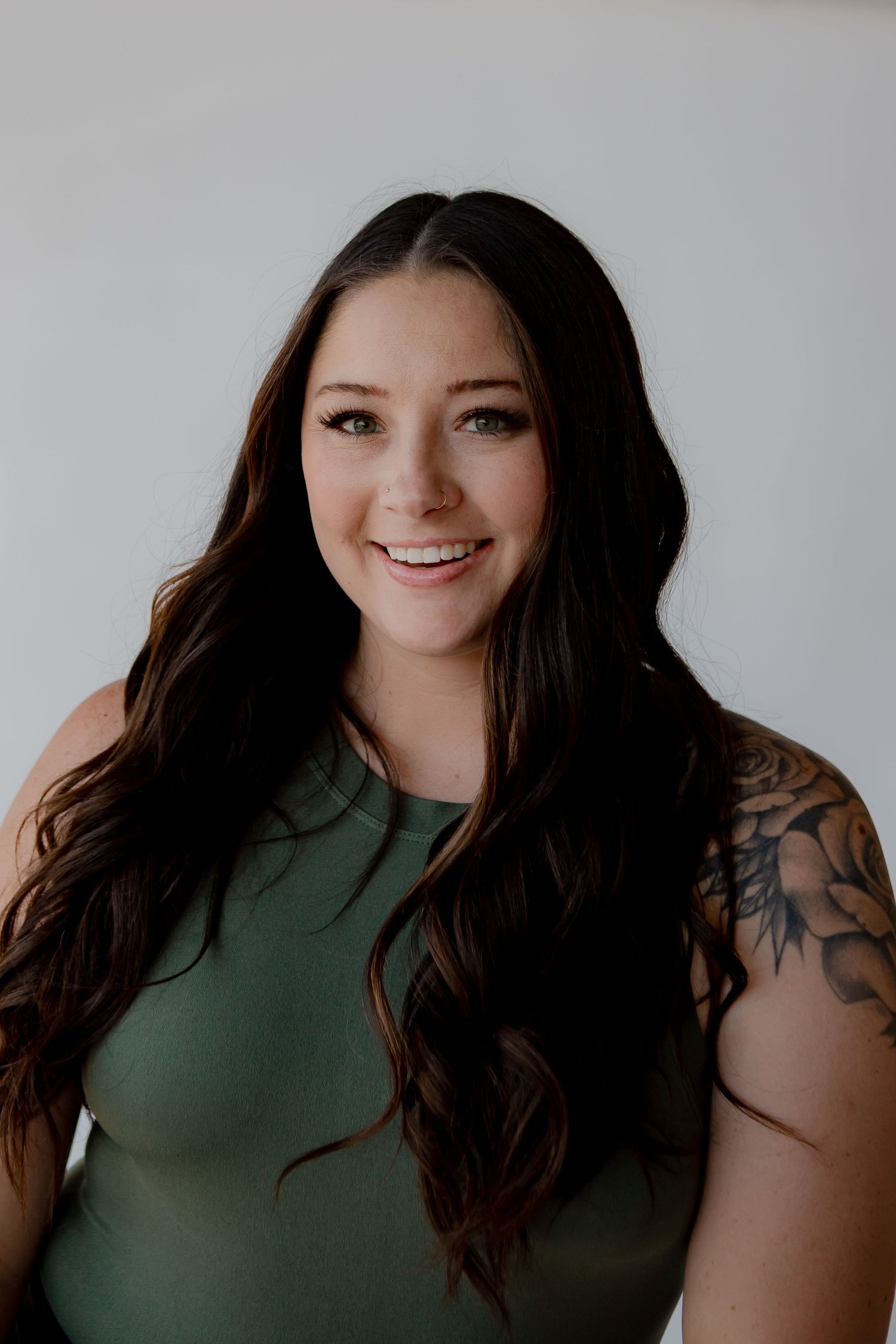 Portrait of a person in a green top with dark hair and tattoos against a white background.