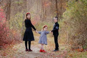 Three children holding hands on a colorful autumn forest path surrounded by fall foliage.