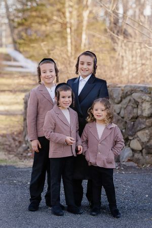 Four boys in matching outfits posing outdoors near a stone wall in natural light.