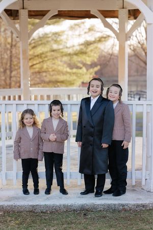Four smiling children standing together under a white gazebo in an outdoor park setting.