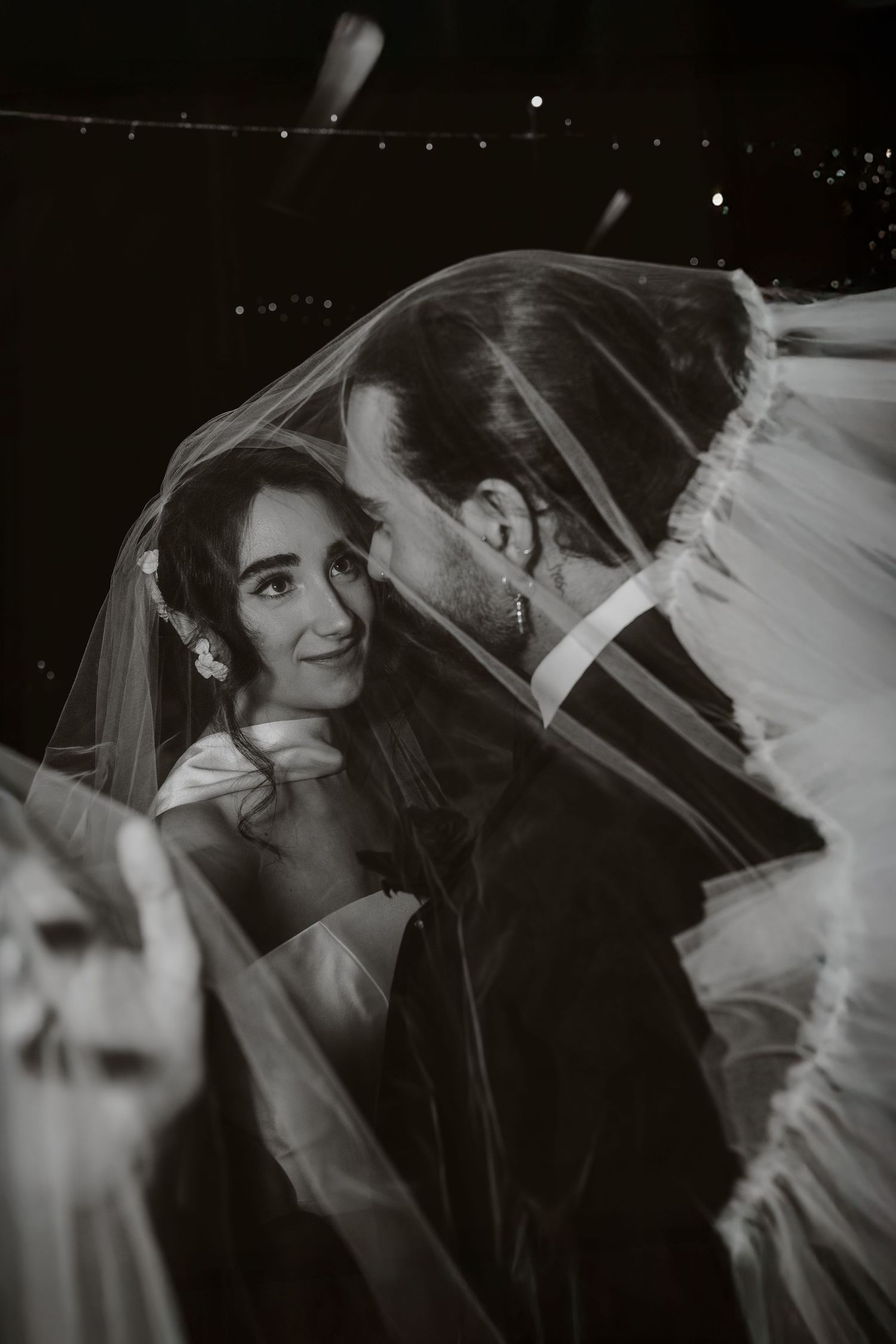 A black and white photo series showing joyful moments through a wedding veil with soft lighting and candid expressions.