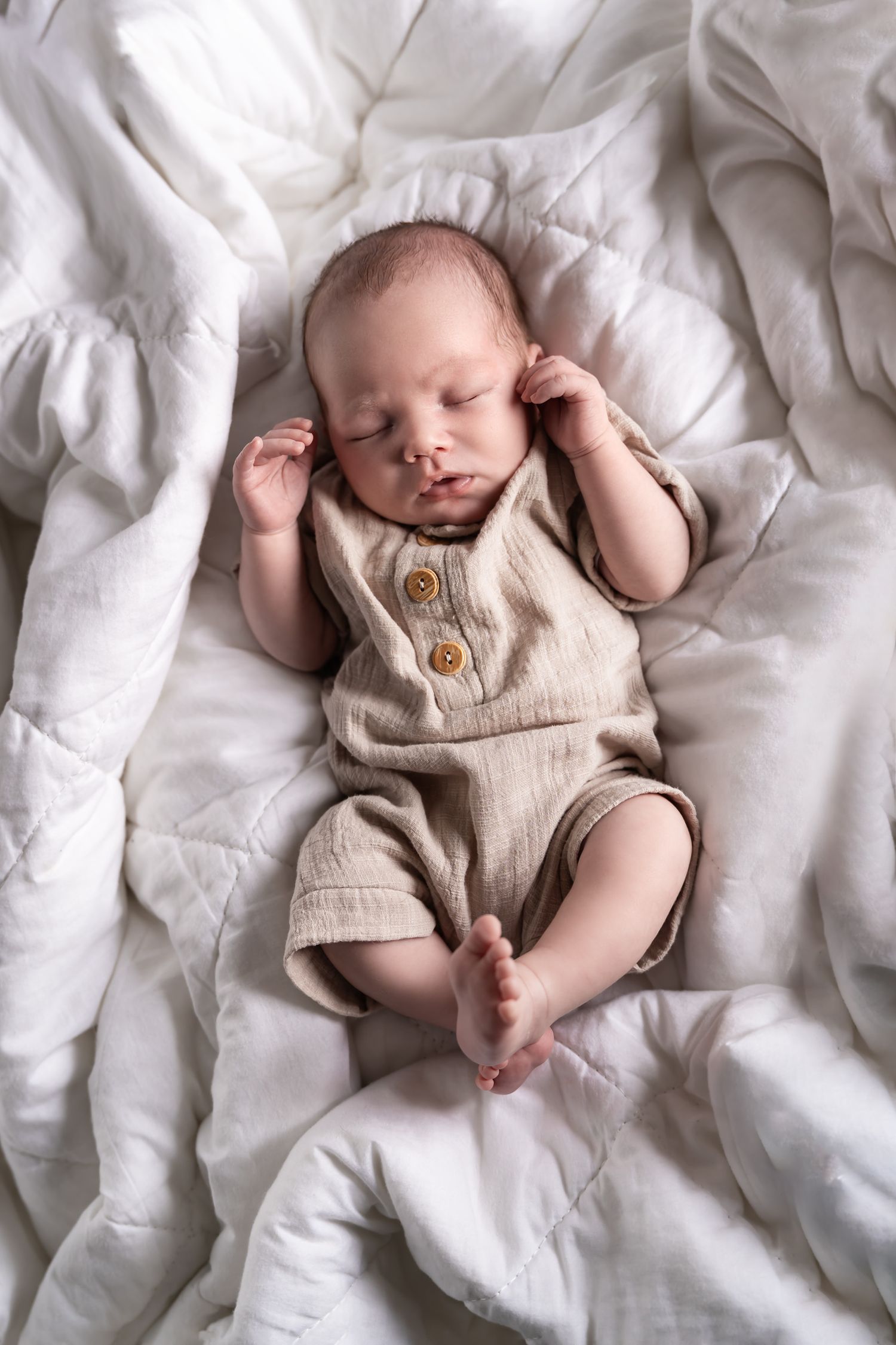 foto van baby tijdens newbornshoot met dekbed als ondergrond
