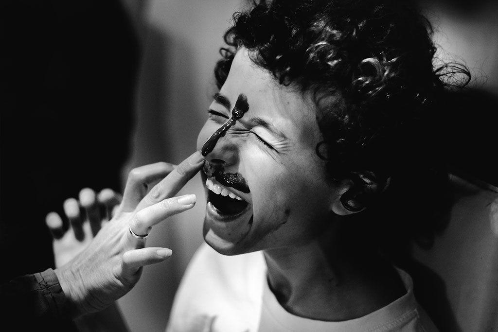 Black-and-white photo of curly hair child laughing when they put line of chocolate from between his eyes till the edge of his nose.