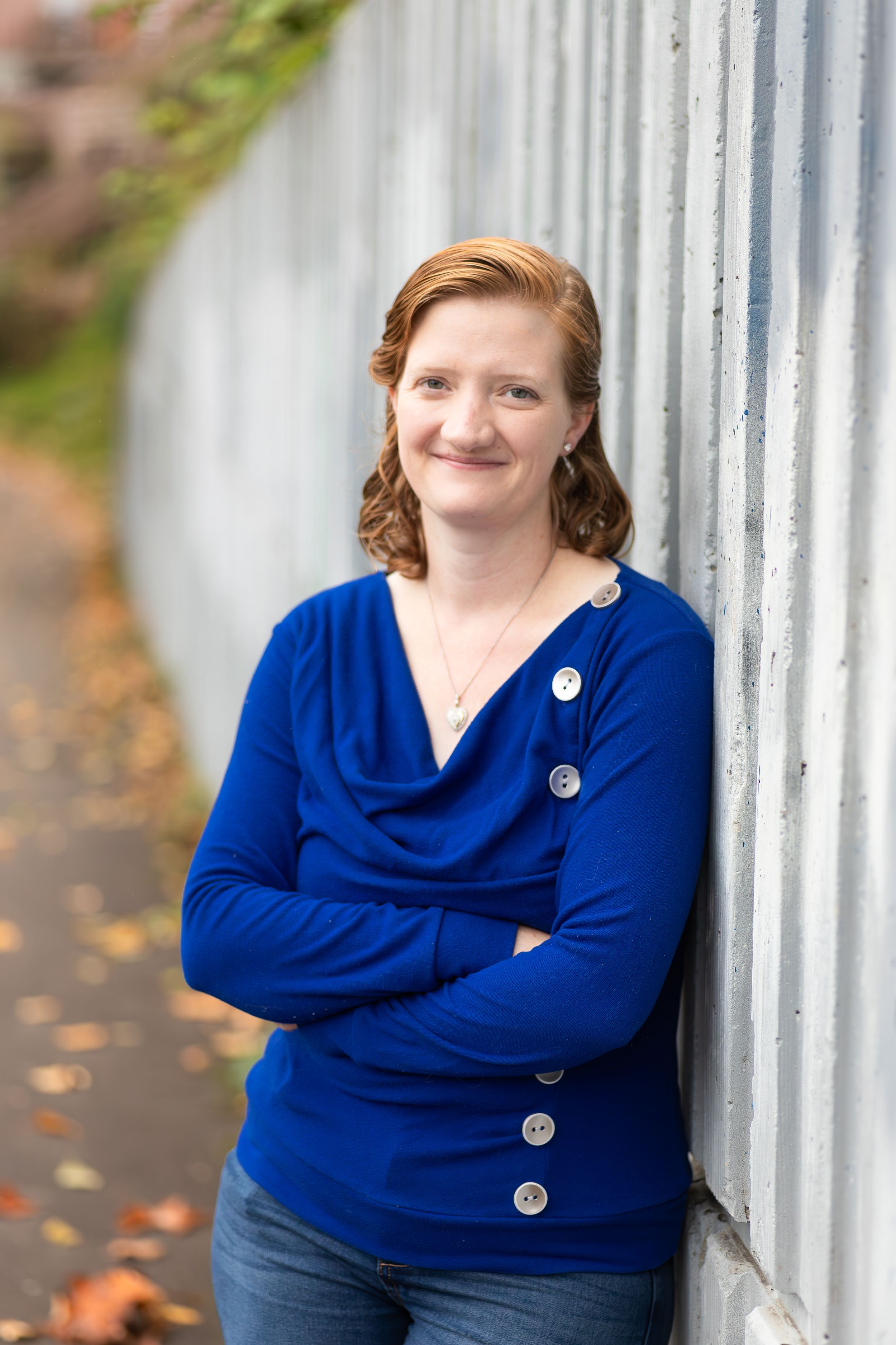 Portrait of person in blue sweater leaning against corrugated wall outdoors.