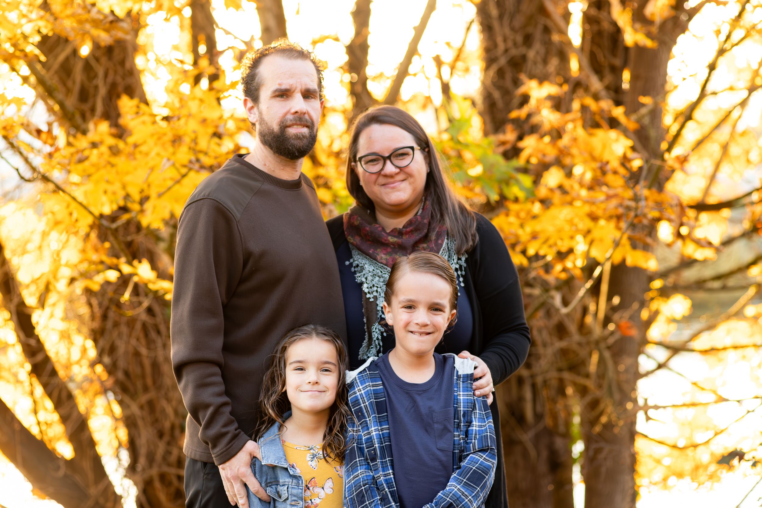 Family of four poses together against vibrant autumn trees with golden leaves.