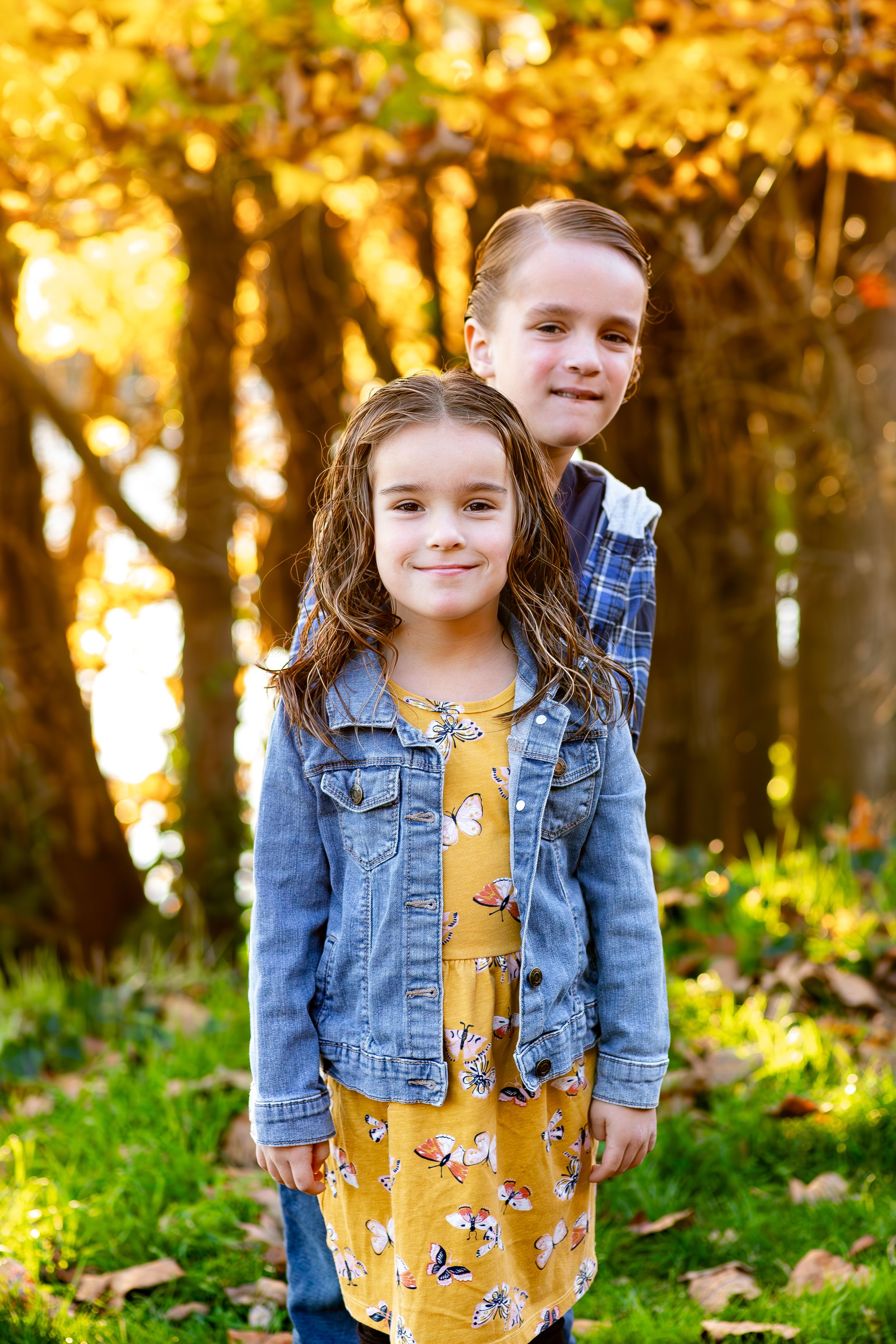 Children posing together against autumn trees with golden sunlight filtering through.